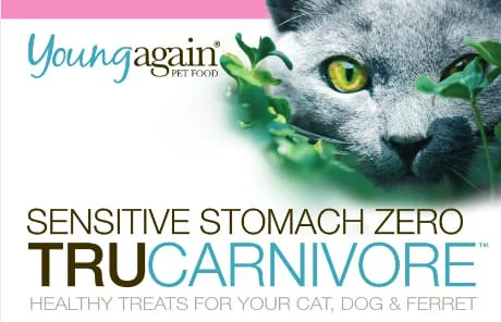 Close-up of a gray cat's face behind green leaves, next to 'Young Again Pet Food.' Below, large text reads TruCarnivore™ Sensitive Stomach Zero Treat—Healthy Treats for Your Cat, Dog & Ferret.